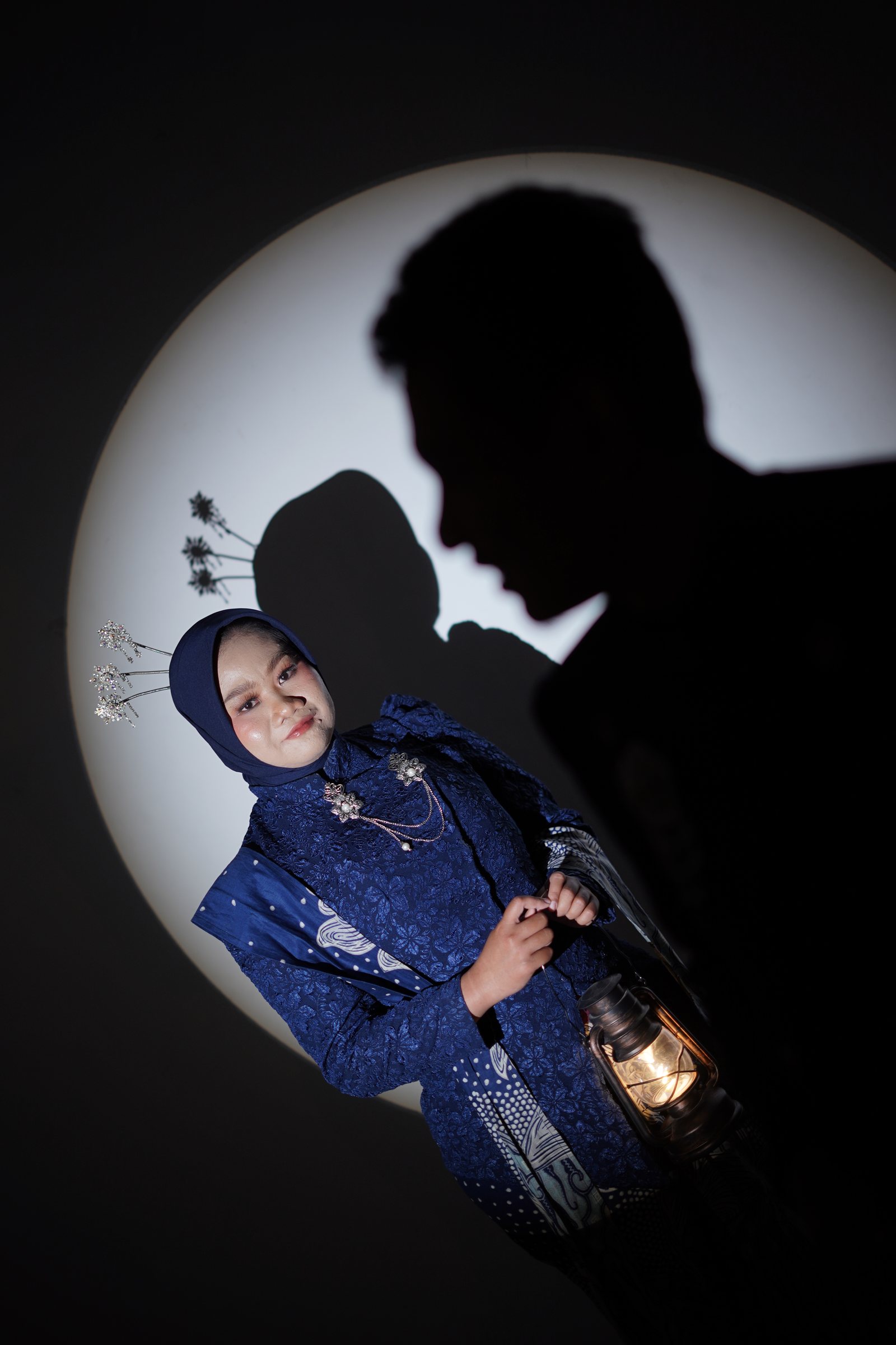 Dewi mengenakan busana biru dengan lantern dan bayangan siluet dalam sesi pre-wedding