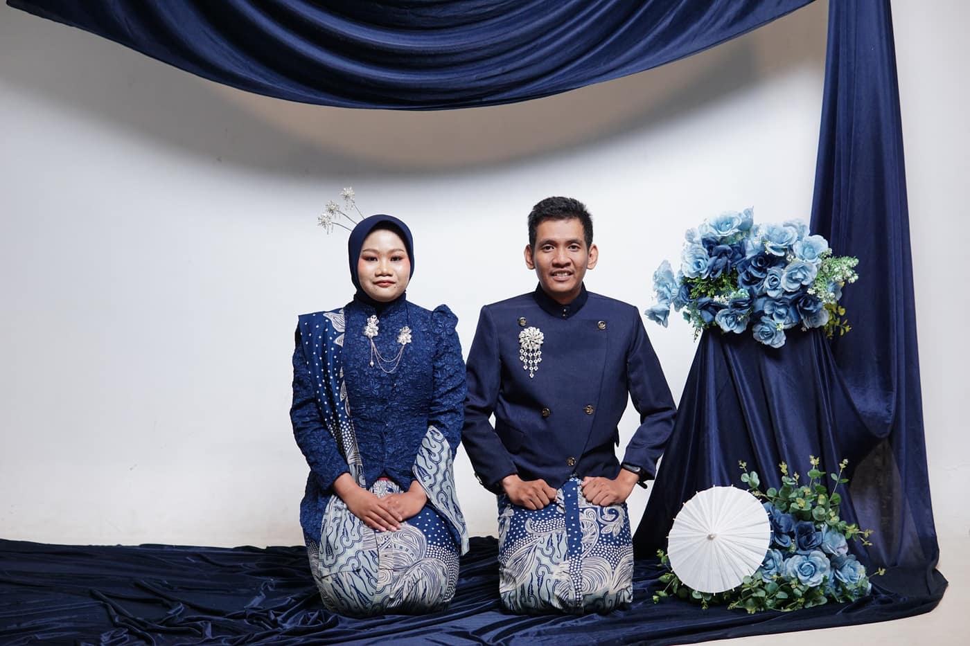 Dewi dan Fadli duduk berdampingan di antara dekorasi biru