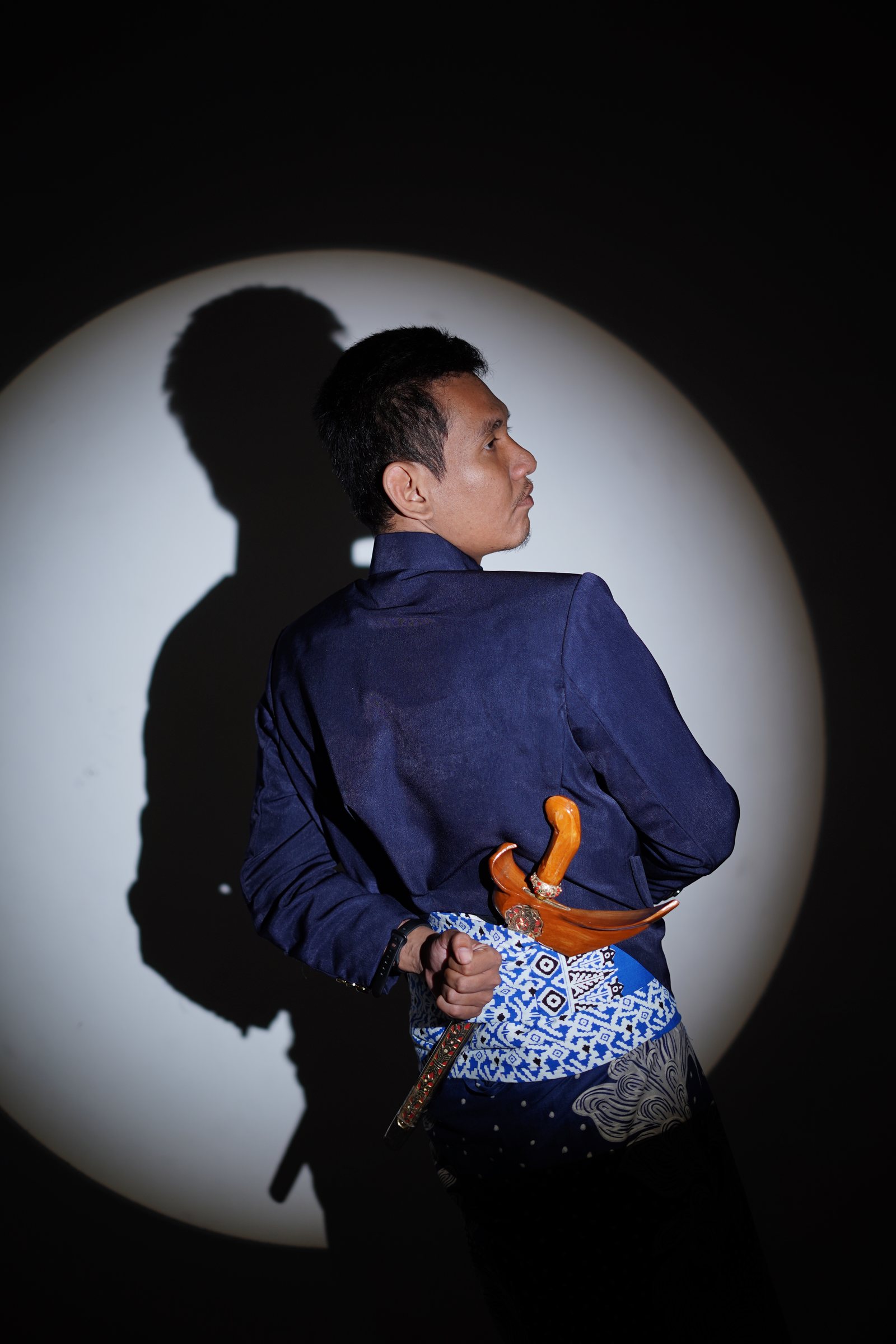 Fadli mengenakan busana navy dengan keris dan bayangan siluet dalam sesi pre-wedding