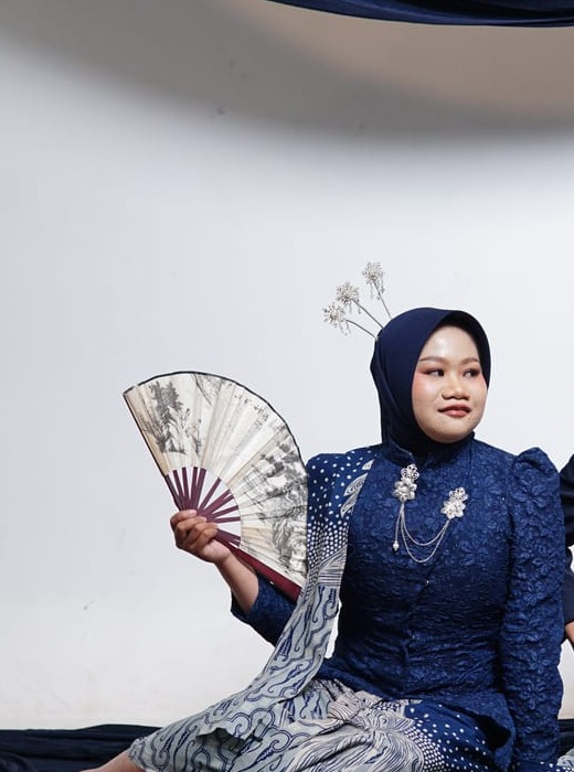 Ula mengenakan busana biru sambil memegang kipas dalam sesi pre-wedding